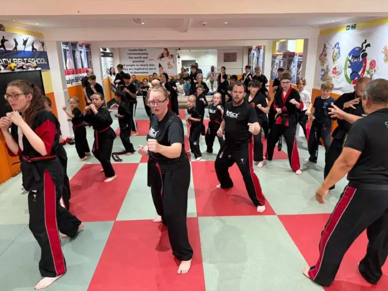 Large group practising martial arts techniques and stances together inside a traditional training studio.