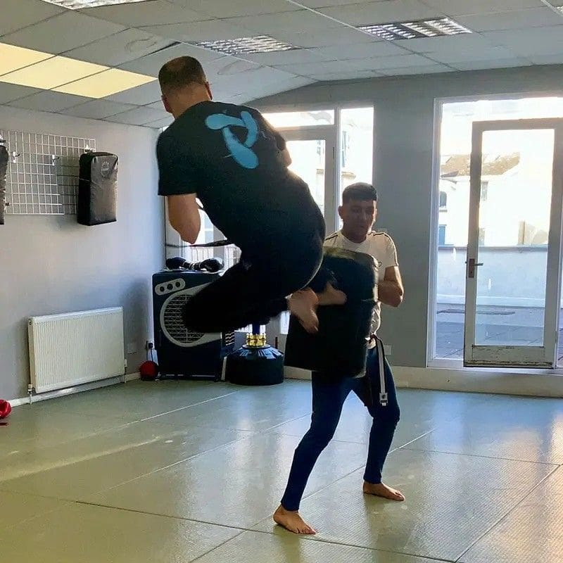 Adult martial arts training session with partner drill and jump kick practice indoors