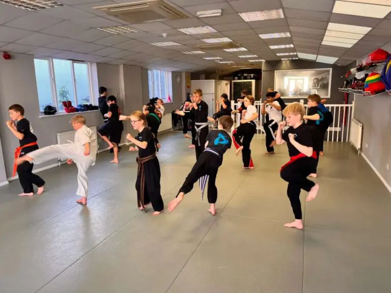 Children practicing martial arts kicks and drills in a bright indoor dojo class
