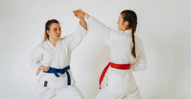 Two teens karate girls in white karate uniforms&mdash;one with a blue belt and one with a red belt&mdash;practicing a defensive blocking technique together.