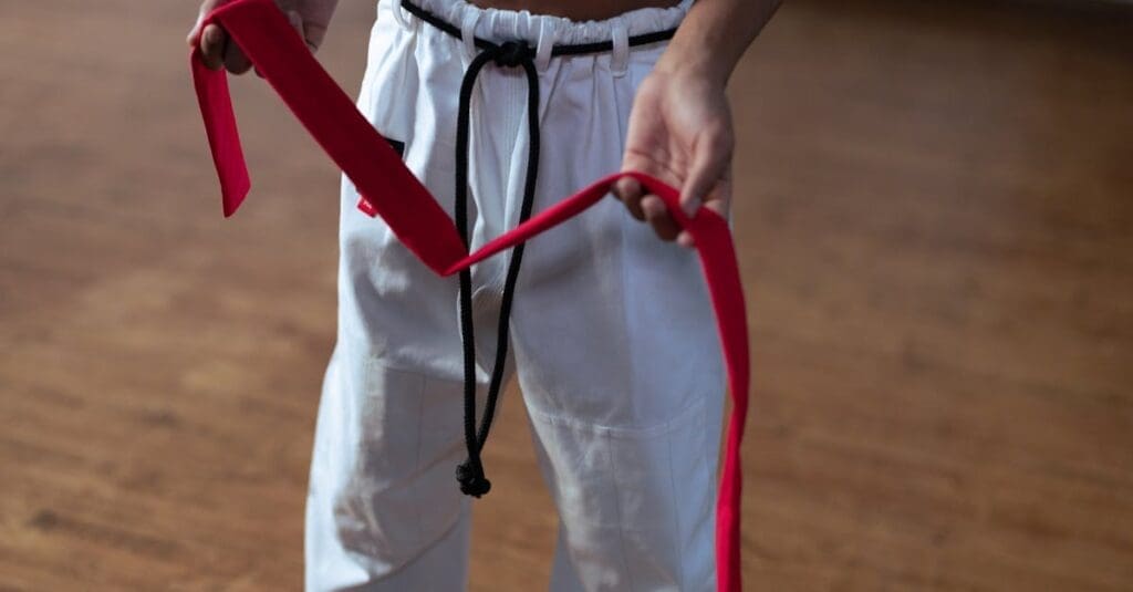 A close-up view of a practitioner tying a red belt around their waist, illustrating proper uniform preparation in a Teen Taekwondo Training Guide.